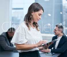 Getting all her tasks done the efficient way. a young businesswoman using a digital tablet in an office with her colleagues in the background.