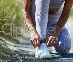 Readying herself for a serious run out in nature. Closeup shot of an unrecognisable woman tying her shoelaces while exercising outdoors.