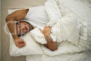 Im struggling to fall asleep. a young man frowning while lying in his bed.