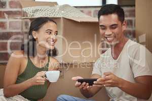 Lets invite our friends and family over to our new home. a man using his cellphone while sitting with his girlfriend in their new home.