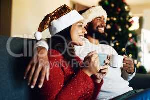 Hot chocolate and happy Christmas memories. a happy young couple relaxing on the sofa and having warm drinks during Christmas at home.