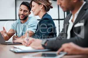 Hes always willing to lend a hand. two young businesspeople talking in the boardroom during a meeting with their colleagues.