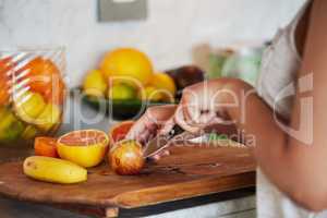 Nutrients and knife collide. an unrecognizable woman slicing fruit and preparing breakfast in the kitchen at home.