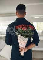 Can you guess whats behind my back. a young man holding flowers behind his back at home.