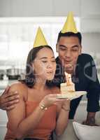 Make a wish. a young couple blowing out candles on a piece of cake at home.