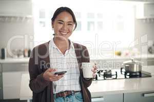 Im taking it easy today. Portrait of a young woman using a cellphone while drinking coffee in the kitchen at home.