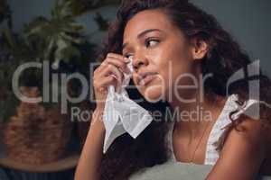 No one has it all together, all the time. a young woman wiping her tears with a tissue while sitting at home alone.