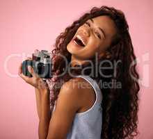 I like to shoot things... with my camera. Studio shot of a young woman laughing while holding her camera.