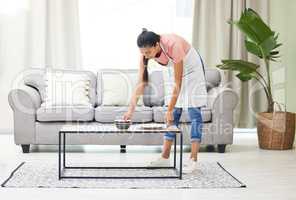 Cleaning up the mess from last nights binge-watching session. a young woman removing dirty dishes from a coffee table in the living room at home.