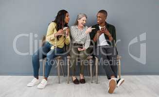 Teeth chattered rhythms. a group of people laughing at a funny visual from a smartphone against a grey wall.