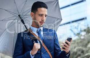 Messages on the move. a handsome young businessman with an umbrella on his morning commute into work.