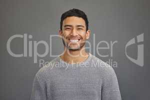 A smile is the best gift you can give someone. a handsome young man standing against a grey background.