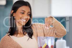 Meet your nutritional goals with a daily smoothie. a young woman preparing a healthy smoothie at home.