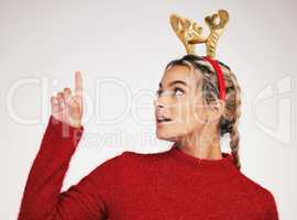 Who can feel the Christmas spirit. Studio shot of a young woman pointing against a grey background.