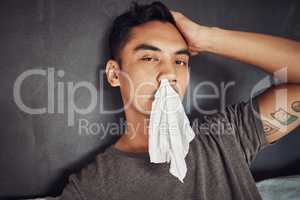 Thanks flu, its not like I had things to do. a young man blowing his nose while recovering from an illness in bed at home.