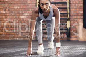 You can read all the determination in her eyes. Portrait of a sporty young woman in starting position in a gym.
