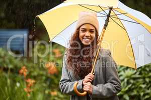 Rainy day walks in the park are the best. a young woman standing in the rain with an umbrella.