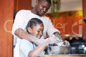 Let me give you a helping hand. a father teaching his daughter how to bake in the kitchen at home.