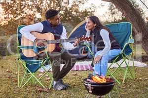Live ,love ,laugh ,camp. a you man playing his guitar to his wife outside while camping.