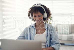 Setting the tone for work. an attractive young woman sitting alone at home and using her laptop while wearing headphones.