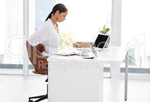 Trying to stay productive. a young businesswoman sitting at a desk looking tired in a modern office.
