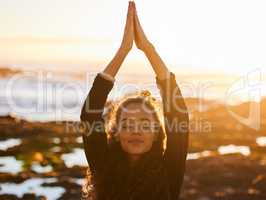 Gather good energy from the universe. an attractive young woman doing yoga alone on the beach at sunset.
