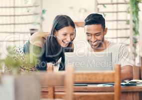 Happy, laughing and casual couple watching or looking at a funny video on a laptop together in a restaurant during day time. Young boyfriend and girlfriend sharing relationship status on social media