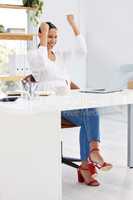 Hard work pays off. a young businesswoman sitting at a desk expressing joy in a modern office.