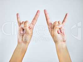 Rock on. Studio shot of a woman making a rock n roll gesture against a grey background.