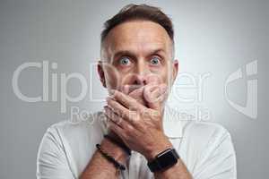 Oops, I wasnt supposed to tell you that. Studio portrait of a mature man covering his mouth and looking shocked against a grey background.