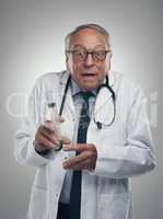 Dont worry this wont hurt. an elderly male doctor holding a syringe for injection in a studio against a grey background.