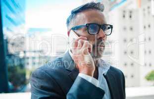 Connecting with clients. Shot a mature businessman using a phone against an urban background.