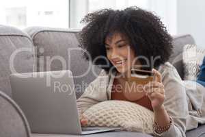 Pay day. a young woman shopping online while laying on the couch at home.