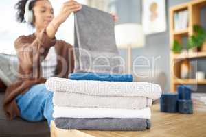 Im almost done with my chores. a woman folding freshly washed towels while sitting on the couch at home.