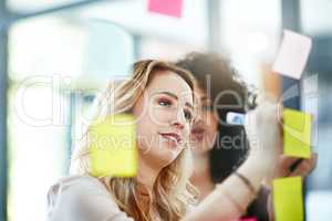 Manager brainstorming, planning and writing sticky notes on glass window. Female worker showing corporate leadership, and management skills. Detail information on tasks to meet company objectives