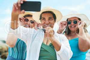 Say cheese, girls. a mature group of friends standing together and using a cellphone to take a selfie on the beach.