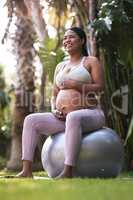 My baby is just as active as I am. a pregnant woman sitting on a stability ball outside.