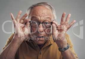 I can see clearly now. Studio shot of an elderly man adjusting his spectacles against a grey background.