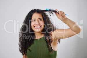 I need to create a better haircare regime. a woman frowning while combing her hair against a grey background.