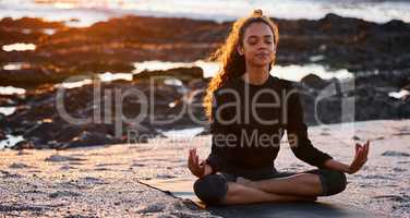 Gratitude brings positive change. an attractive young woman sitting alone on a mat and meditating on the beach at sunset.