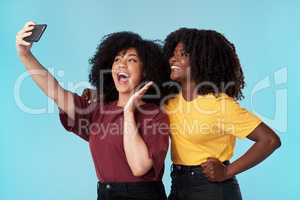 Worlds best friends at it again. Studio shot of two young women using a smartphone to take selfies against a blue background.