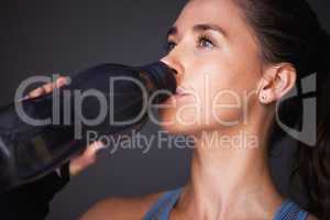 Hydration is key for peak performance. a sporty young woman drinking water against a grey background.