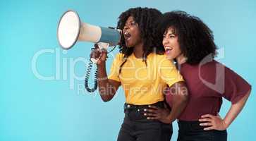Take a stand, make a change. Studio shot of two young women using a megaphone against a blue background.
