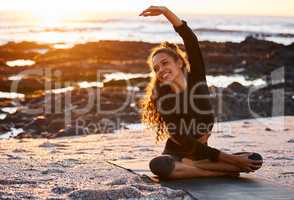 Moving to the sound of the waves. an attractive young woman sitting on a mat and stretching while doing yoga on the beach at sunset.