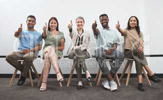 Believe in yourself and you will succeed. Portrait of a group of businesspeople showing thumbs up while sitting together in a line against a white wall.