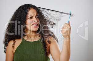 Why must this always be such a struggle. a woman frowning while combing her hair against a grey background.