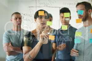 Designers planning a strategy for a group project on a glass whiteboard together in a meeting. Creative, confident and professional young men and women writing smart ideas down together as a team