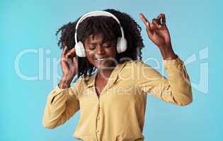 Dance to the rhythm of your heart. Studio shot of a young woman using headphones and dancing against a blue background.