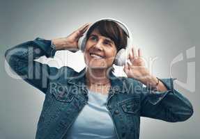 I remember when I used to boogy to this beat. Studio shot of a senior woman wearing headphones against a grey background.