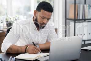 Busy with some big plans in the making. a young businessman writing notes while working on a laptop in an office.